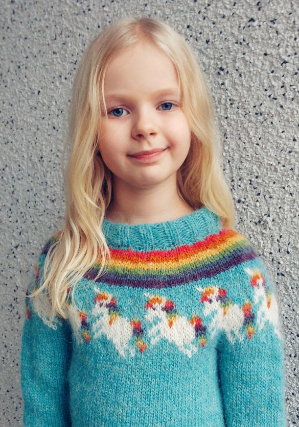 Girl wearing a rainbow unicorn knitted sweater. The pattern is available on Ravelry.com.