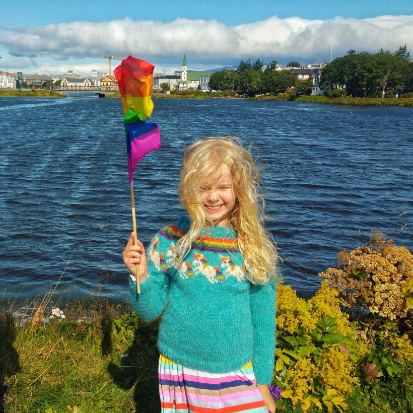 Girl wearing a rainbow unicorn knitted sweater. The pattern is available on Ravelry.com.